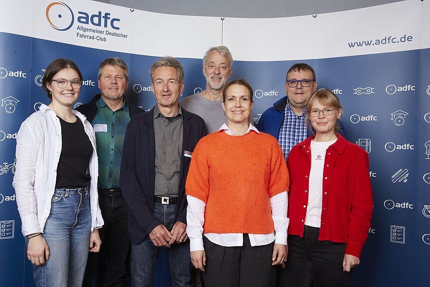 ADFC-Bundesvorstand 2025 Ein Gruppenbild vor einem blauen Hintergund mit ADFC-Logos. Der neue ADFC-Bundesvorstand. Von links nach rechts: Lena Adam, Joachim Lohse, Christian Tänzler, Frank Masurat, Sarah Holczer, Christoph Schmidt und Vera Konrad. Nicht im Bild: Clara Bohle.