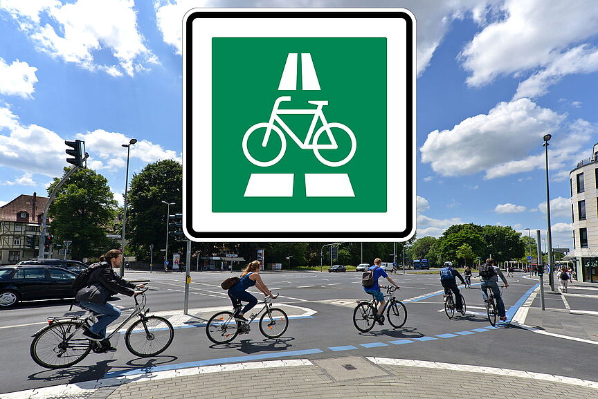 Verkehrszeichen Radschnellweg Quadratisches, grünes Verkehrsschild mit weißem Rand. In der Mitte ist ein weißes Fahrrad-Symbol abgebildet. Darüber und darunter deuten weiße Balken eine Fahrbahn an. Im Hintergrund fahren mehrere Personen auf Fahrrädern über eine Kreuzung.